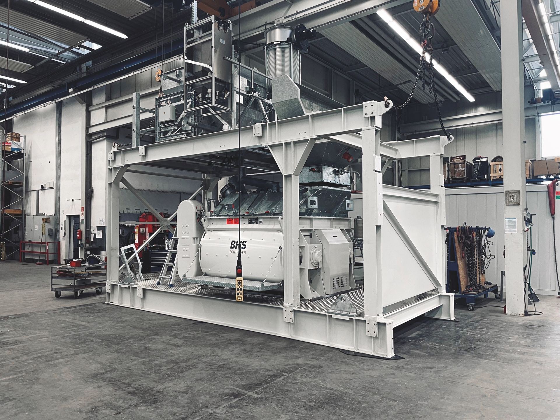 A finished NISBAU twin-shaft mixing plant rigged to the crane in the works hall in Germany
